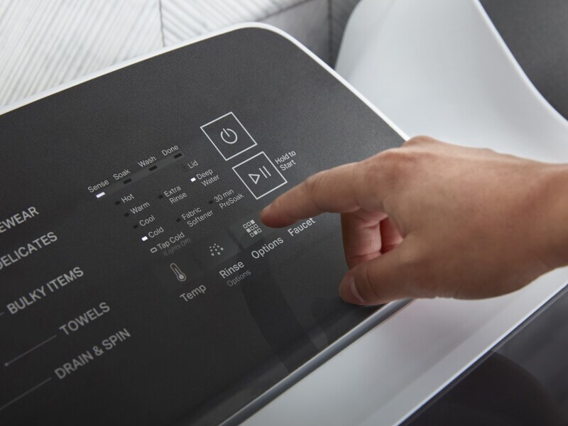 A person’s hand, operating the control panel of their washing machine