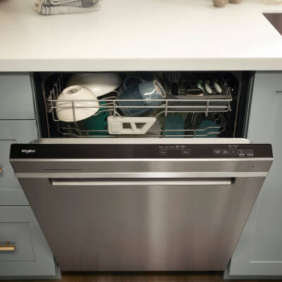A partially opened Whirlpool® dishwasher with dishes inside