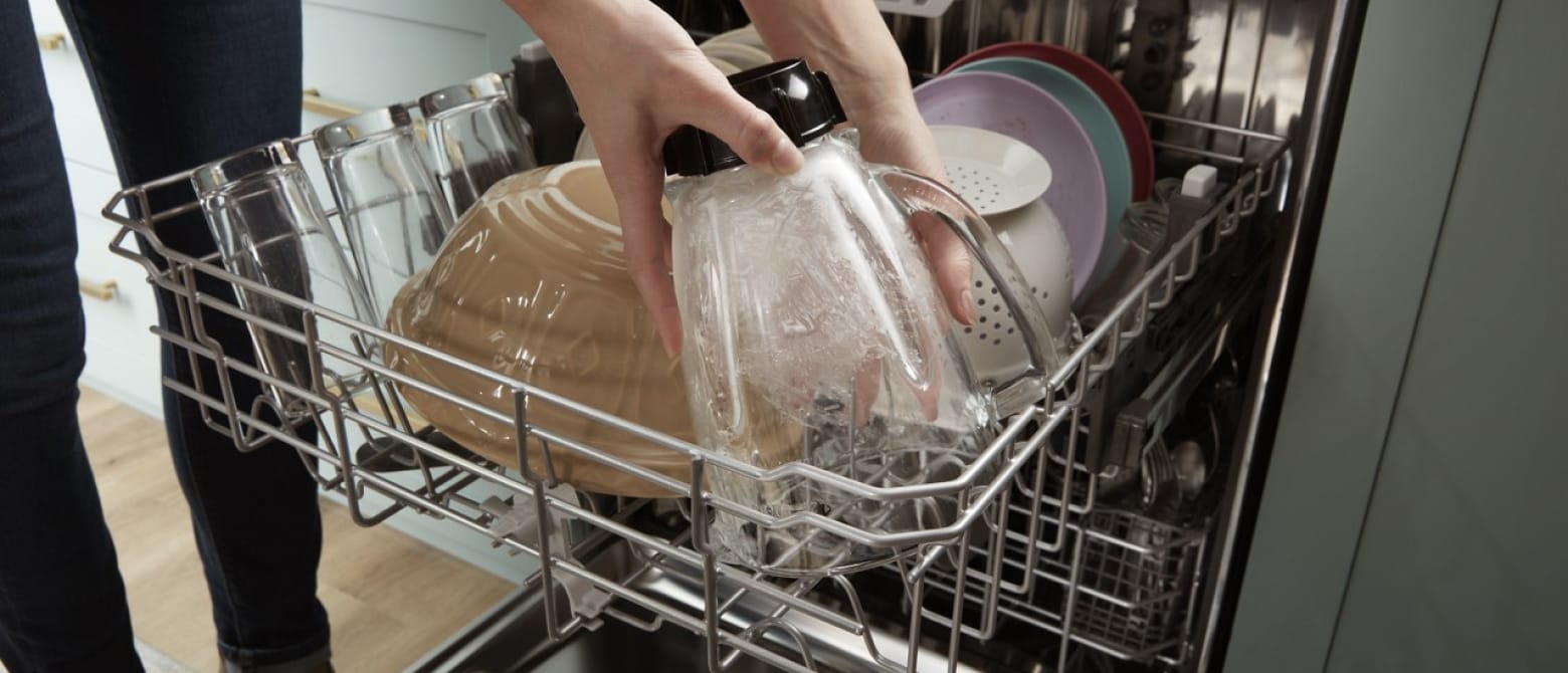 A person loading a blender jar into a dishwasher A person loading a blender jar into a dishwasher