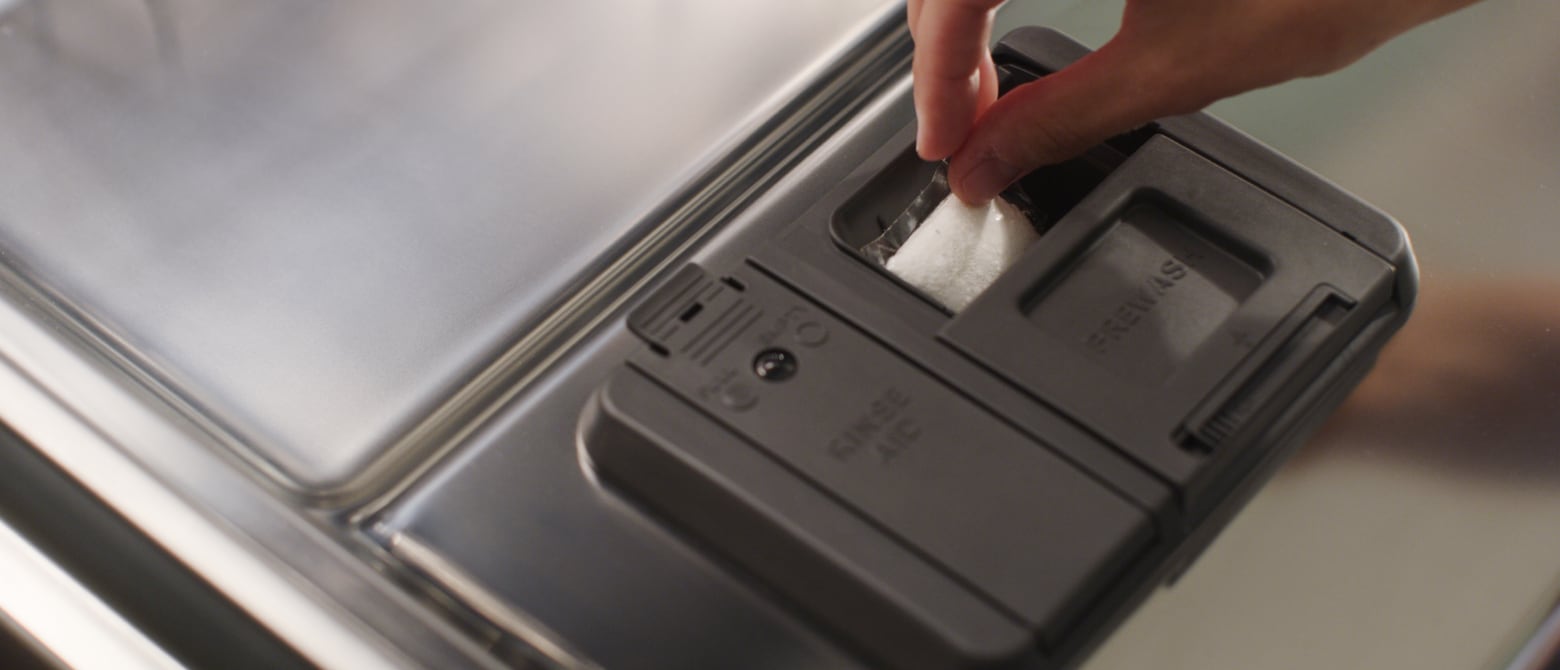 A hand placing a dishwasher detergent pod into a dispenser A hand placing a dishwasher detergent pod into a dispenser