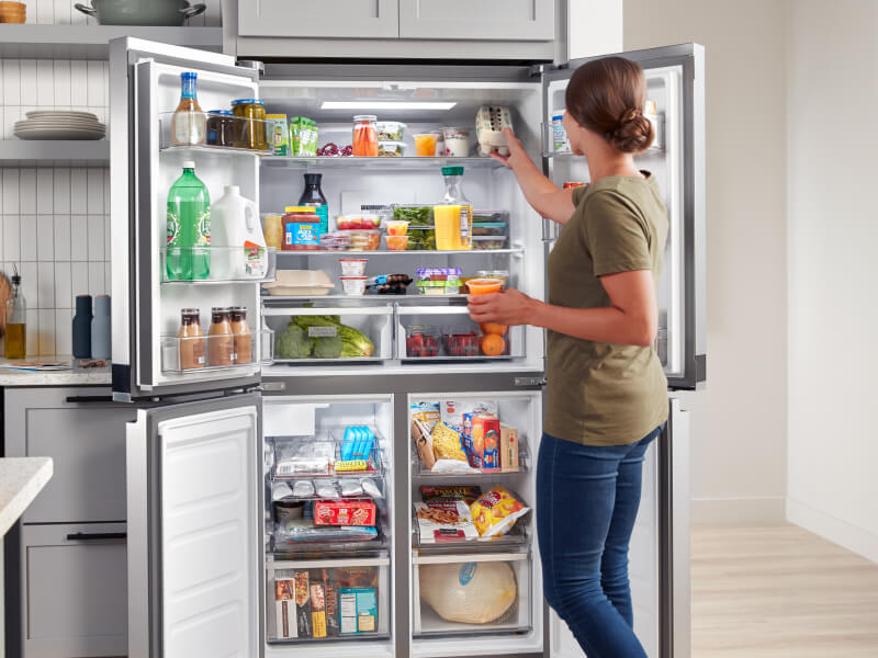 A person putting food in her open refrigerator A person putting food in her open refrigerator