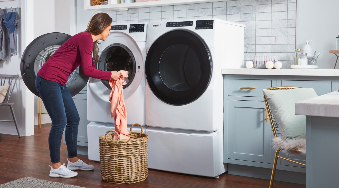 Person transferring laundry from a wicker basket into a white front load washer Person transferring laundry from a wicker basket into a white front load washer
