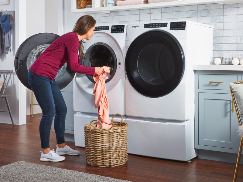 Person transferring laundry from a wicker basket into a white front load washer Person transferring laundry from a wicker basket into a white front load washer
