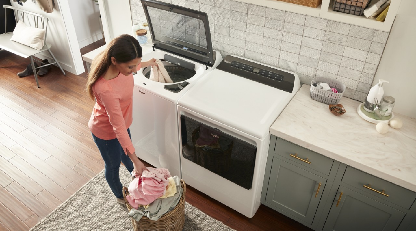 Person loading clothing into white top-load washer