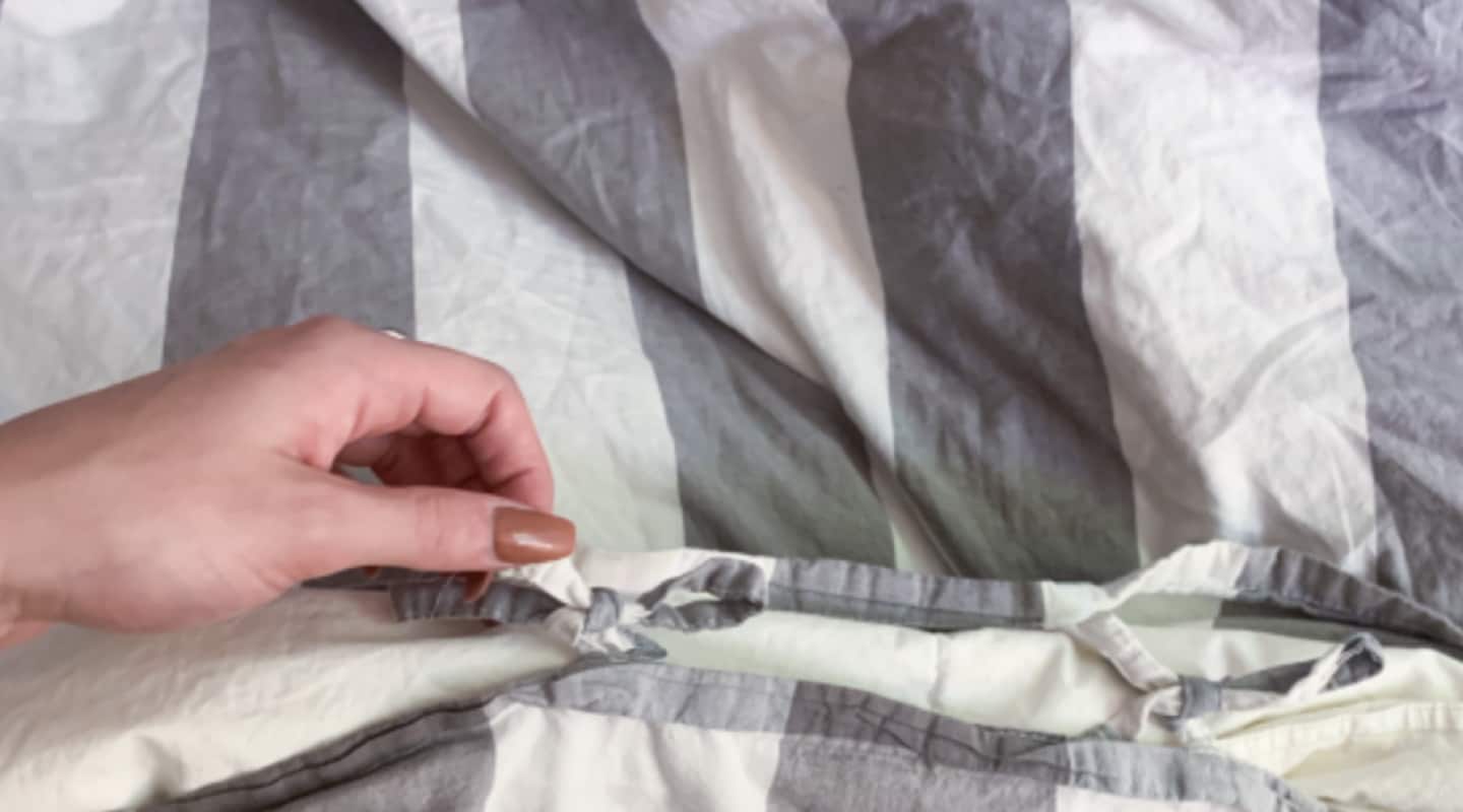Person removing gray and white striped duvet cover from comforter