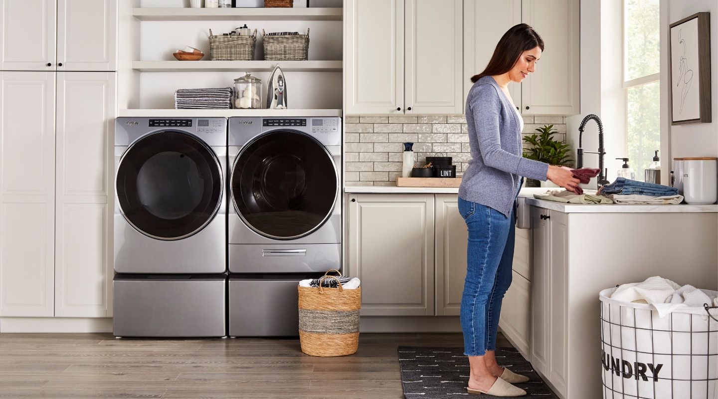 Woman in a laundry room with stainless steel Whirlpool® front load washer and dryer set Woman in a laundry room with stainless steel Whirlpool® front load washer and dryer set