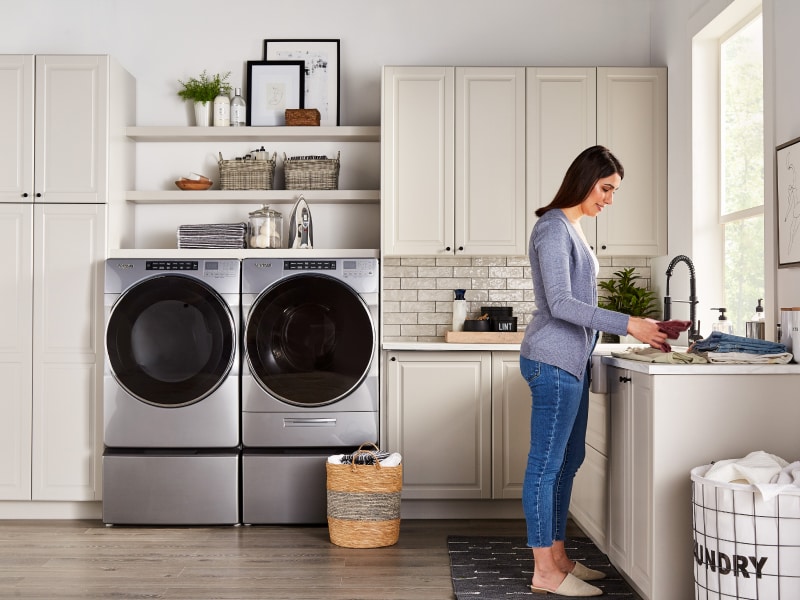 A person folding laundry with a Whirlpool® washer and dryer nearby. A person folding laundry with a Whirlpool® washer and dryer nearby.