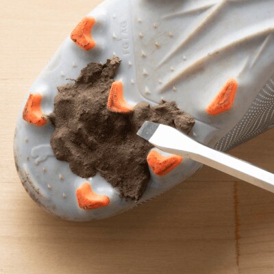 Bottom of a cleat caked with dirt and a screwdriver