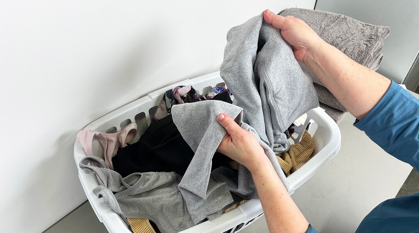 A person holding a pair of leggings above a laundry basket