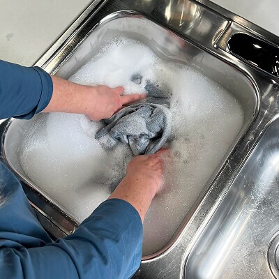 A person gently washing leggings in a sink filled with water and suds