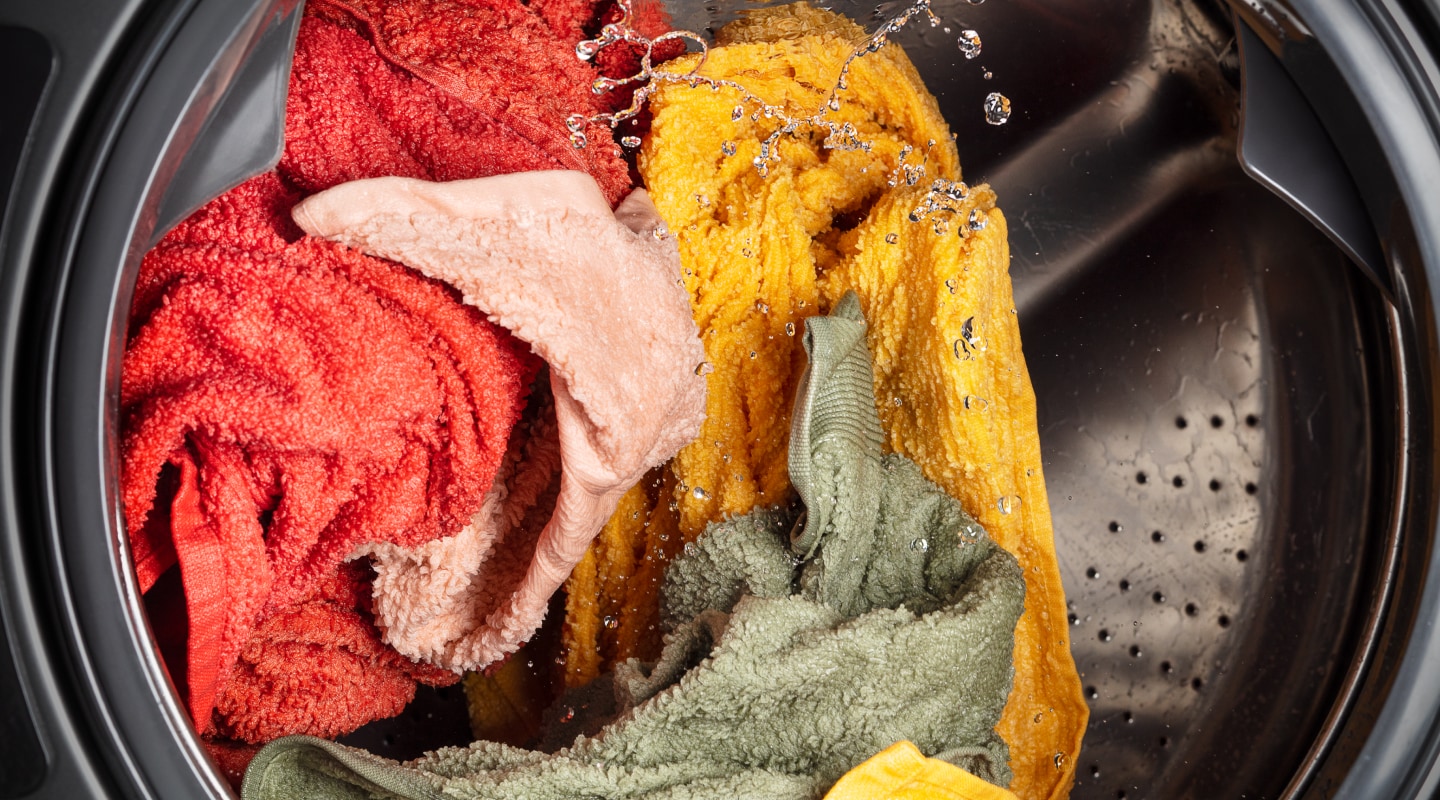 Towels of assorted colors being cleaned in a washing machine  Towels of assorted colors being cleaned in a washing machine