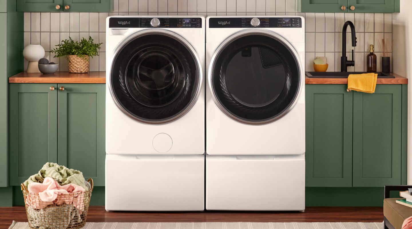 A white Whirlpool® Front Load Washer and Dryer in a laundery room with green cabinetry