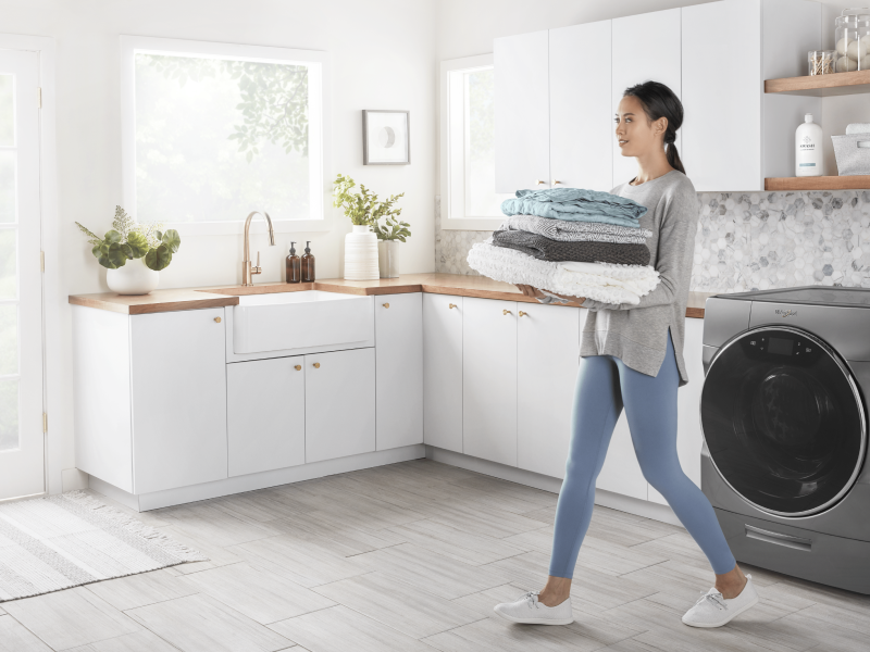 A woman carrying folded laundry cleaned by a Whirlpool® washing machine A woman carrying folded laundry cleaned by a Whirlpool® washing machine