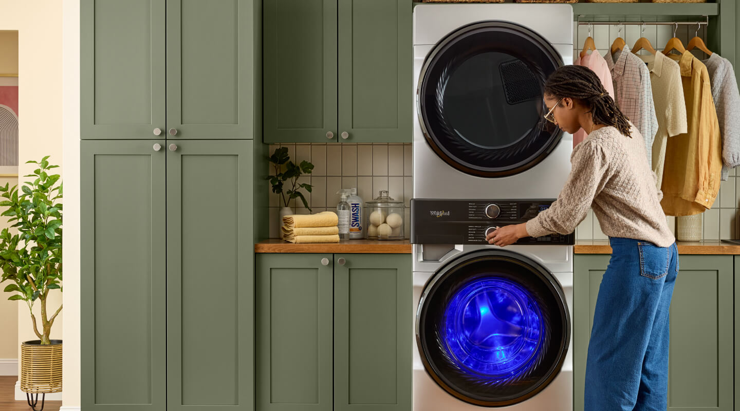 Person selecting settings on a Whirlpool® Front Load Laundry Tower while UV light shines