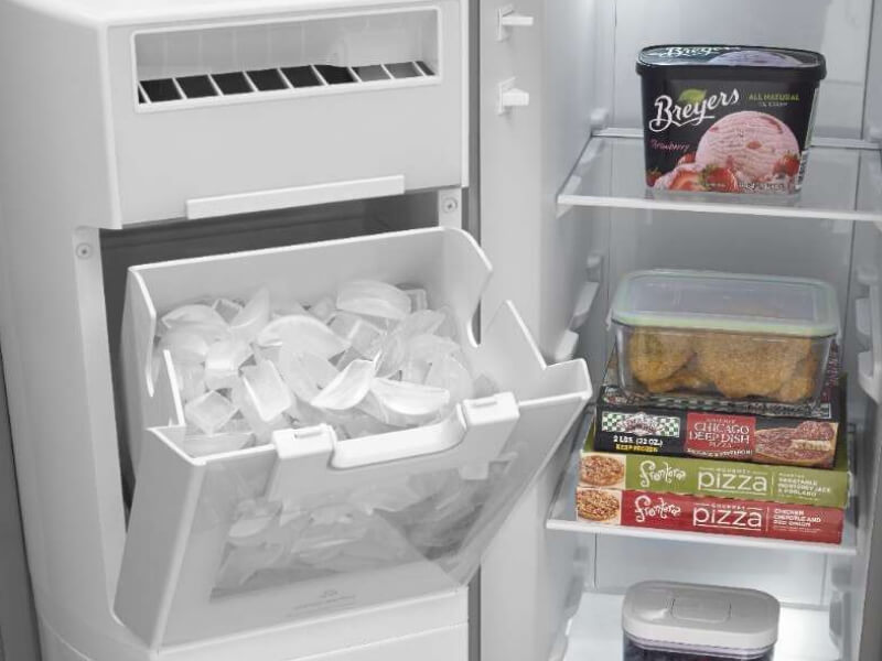 Open freezer door in side-by-side refrigerator revealing open, in-door ice maker