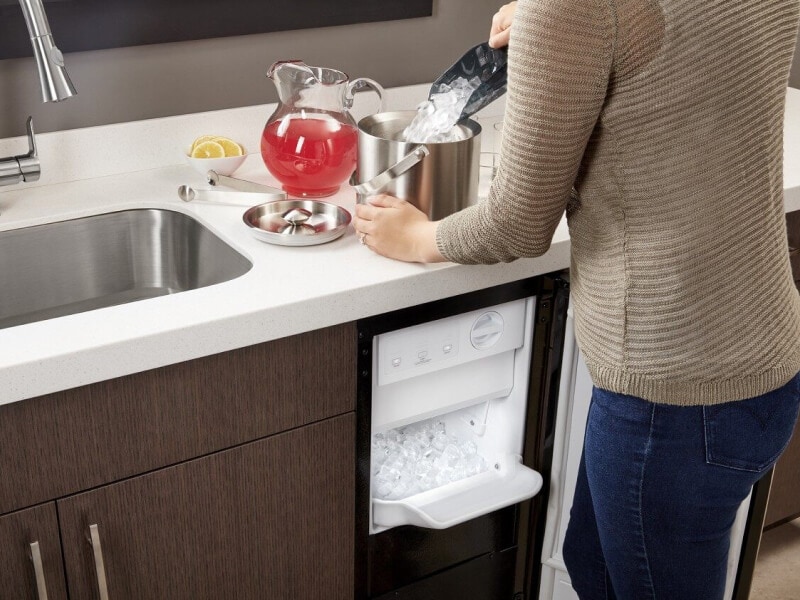 Woman scooping ice out of ice maker and into ice bucket on counter