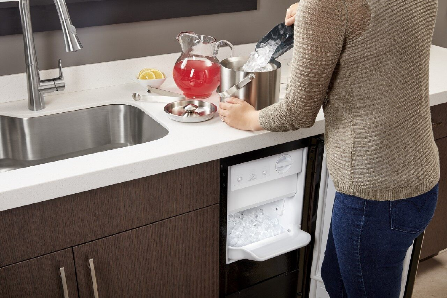 Woman scooping ice out of ice maker and into ice bucket on counter