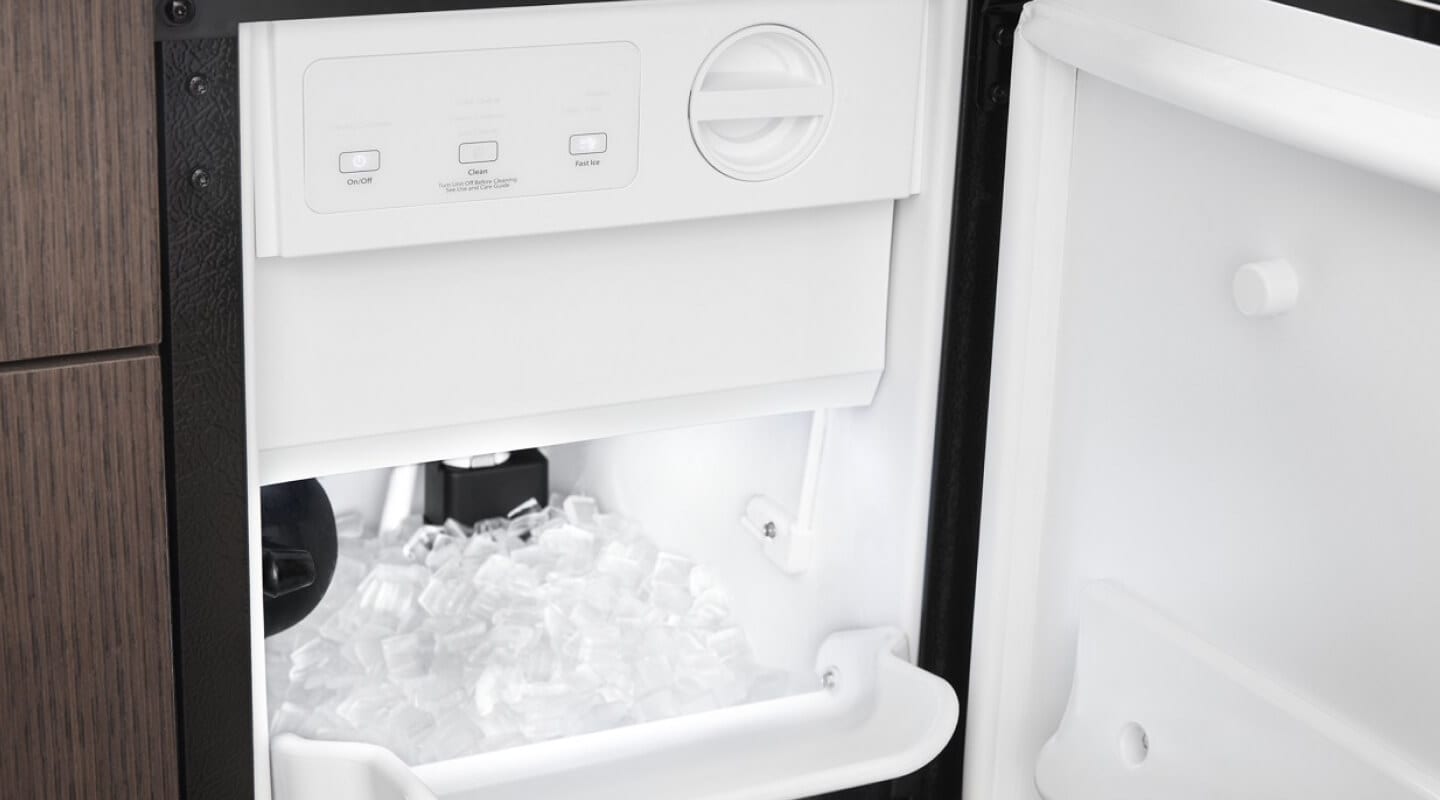 Close-up of open, standalone ice maker installed in brown cabinetry