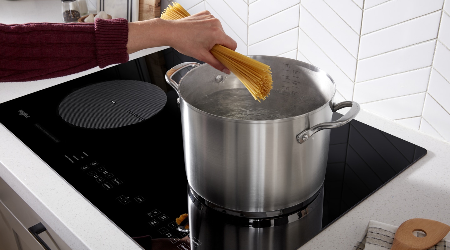 Person adding spaghetti to a stock pot on an induction cooktop Person adding spaghetti to a stock pot on an induction cooktop