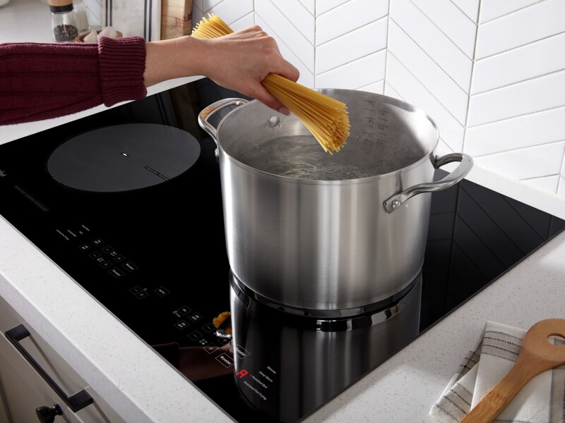 Person adding spaghetti to a stock pot on an induction cooktop Person adding spaghetti to a stock pot on an induction cooktop