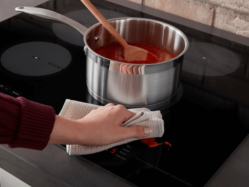Person wiping sauce splatter off of an induction stovetop Person wiping sauce splatter off of an induction stovetop