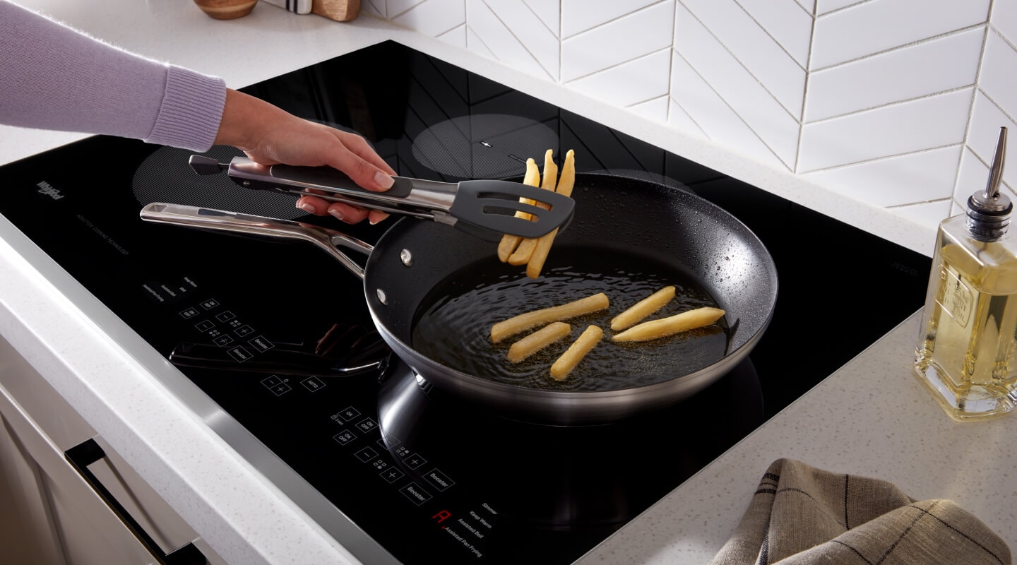 Person frying french fries in a frying pan on top of an induction cooktop Person frying french fries in a frying pan on top of an induction cooktop