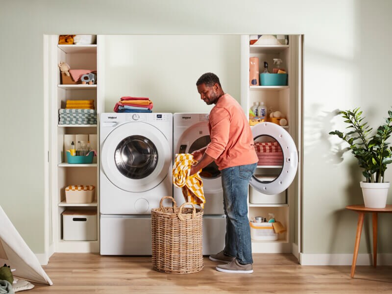 Person placing clothes in laundry basket in front of Whirlpool® Washer and Dryer