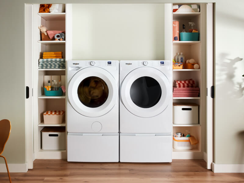 White Whirlpool® Front Load Washer and Dryer on pedestals between shelves