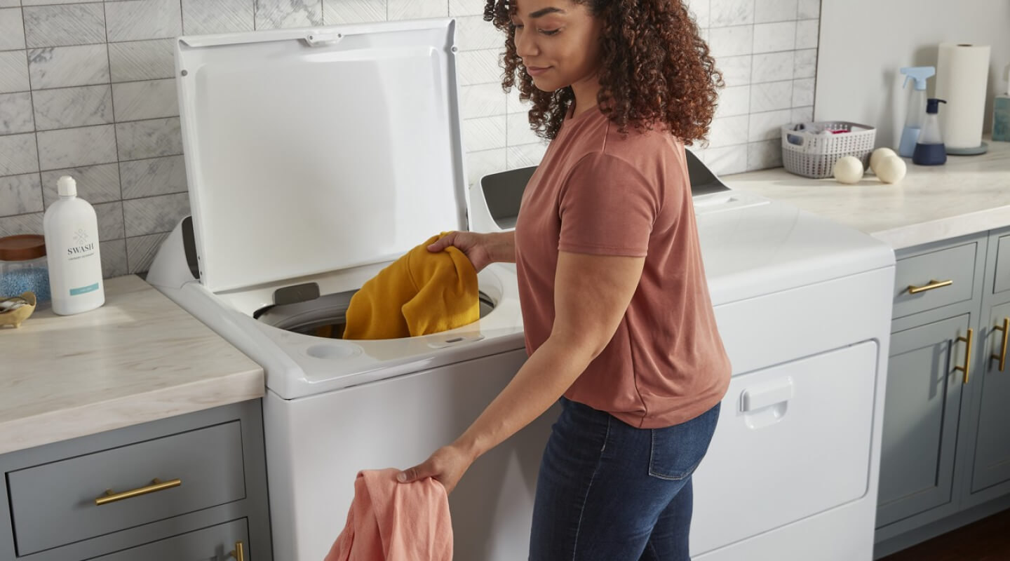 Person adding clothing to a white Whirlpool® Top Load washer