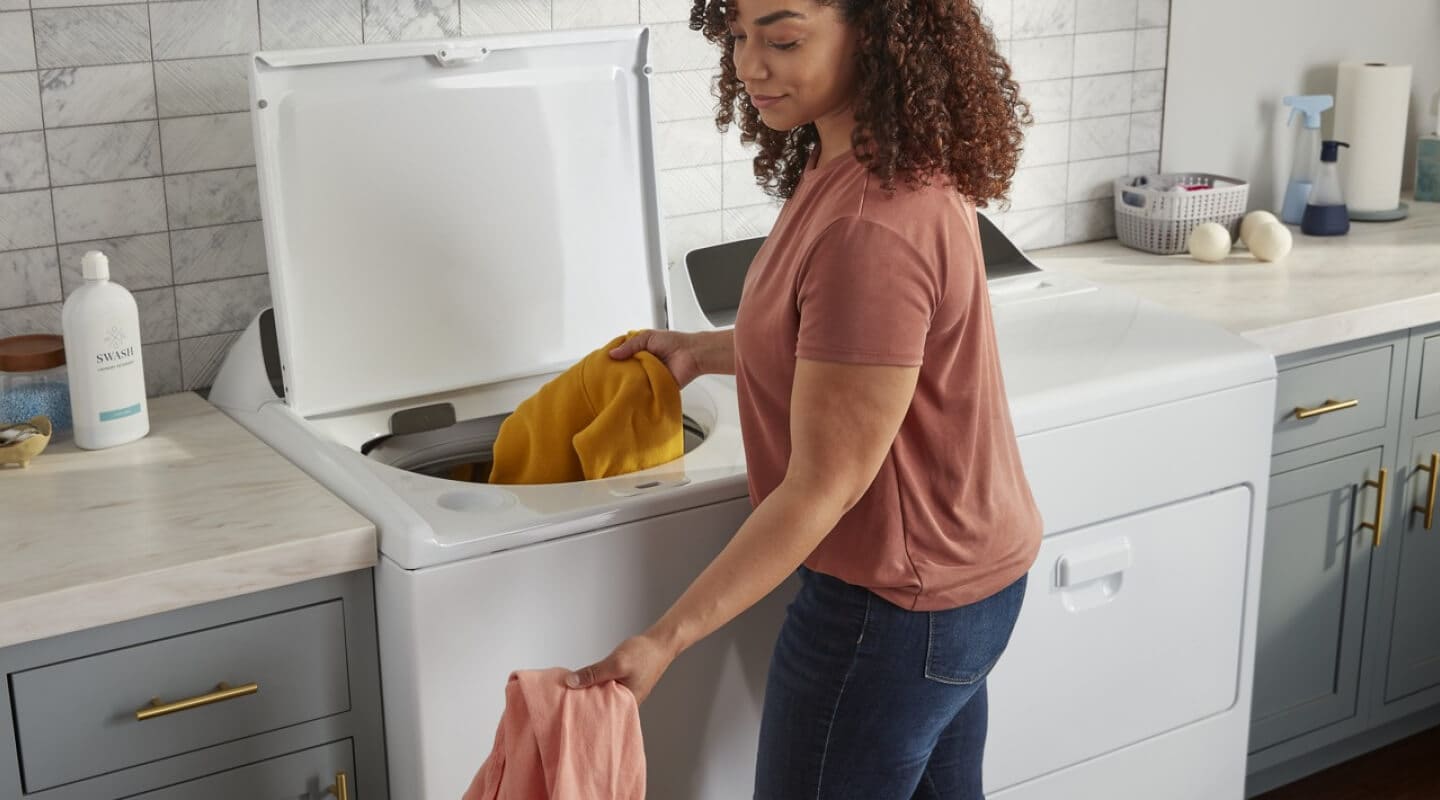 Person adding clothing to a white Whirlpool® Top Load washer