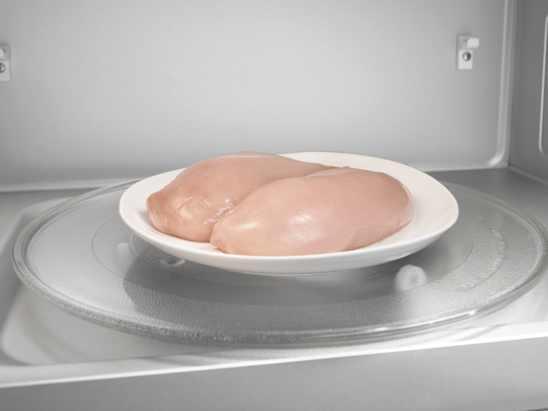 Two chicken breasts on a plate in a microwave Two chicken breasts on a plate in a microwave