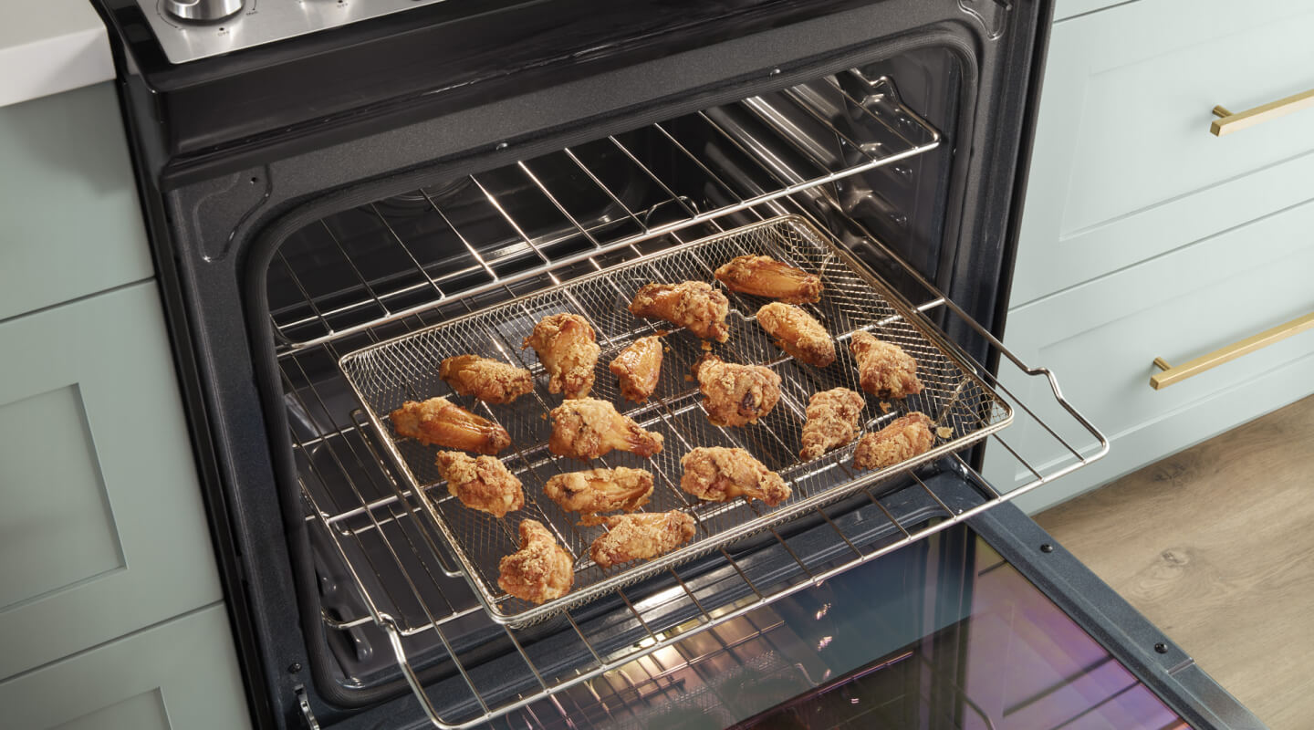 Chicken wings in an air fry basket inside an open oven Chicken wings in an air fry basket inside an open oven
