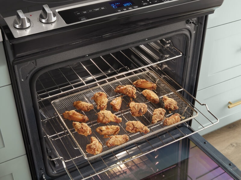 Chicken wings in an air fry basket inside an open oven Chicken wings in an air fry basket inside an open oven