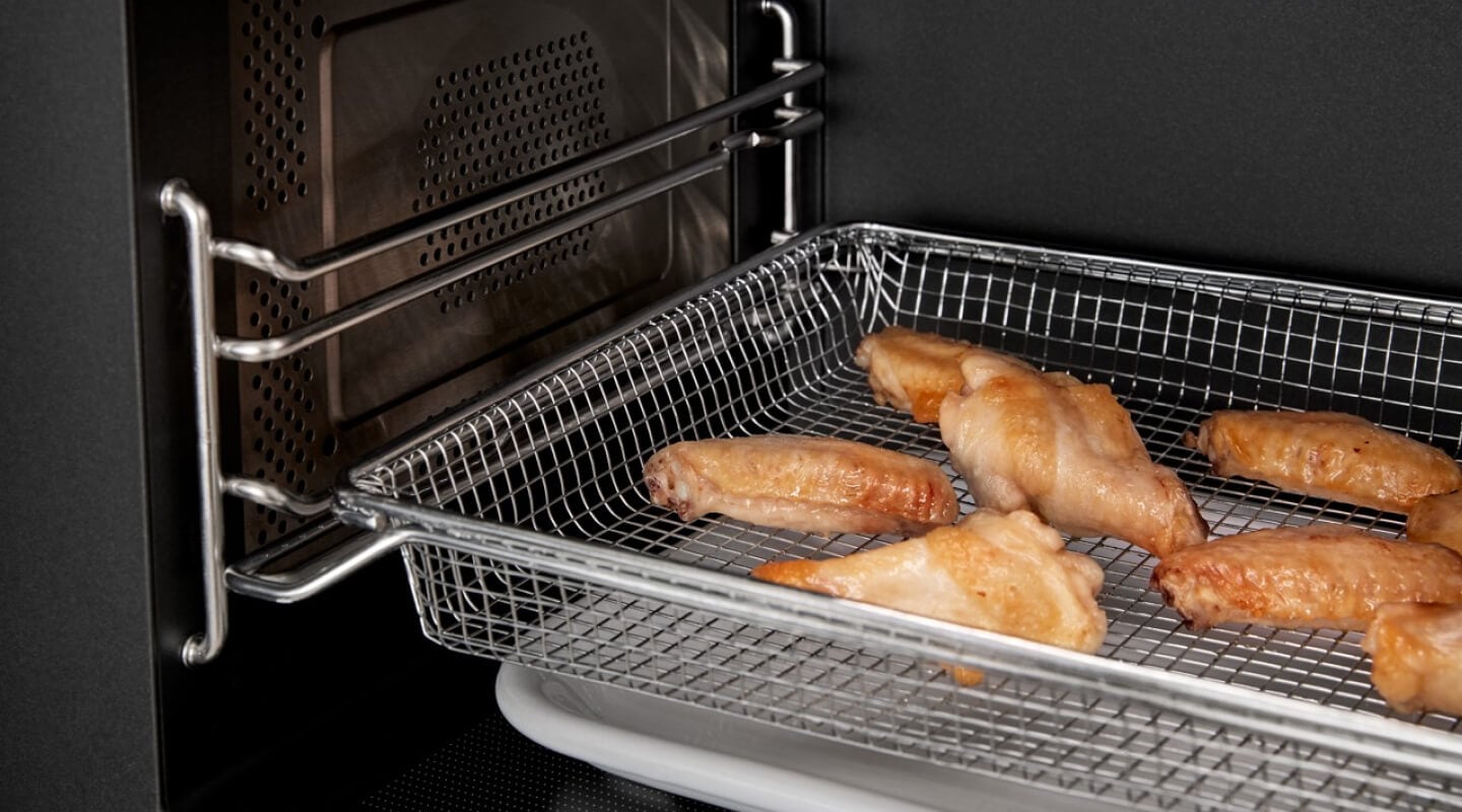 Chicken wings in an air fryer basket inside of the oven