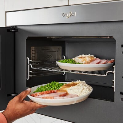 Person loading multiple dishes into and under cooking rack in microwave