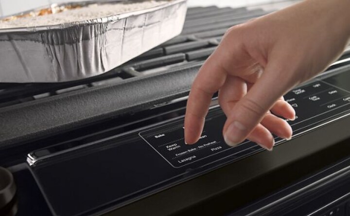 A hand pressing the buttons on a stove to preheat the oven