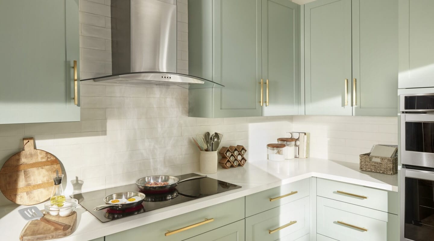 A curved glass island mount range hood above dishes cooking below