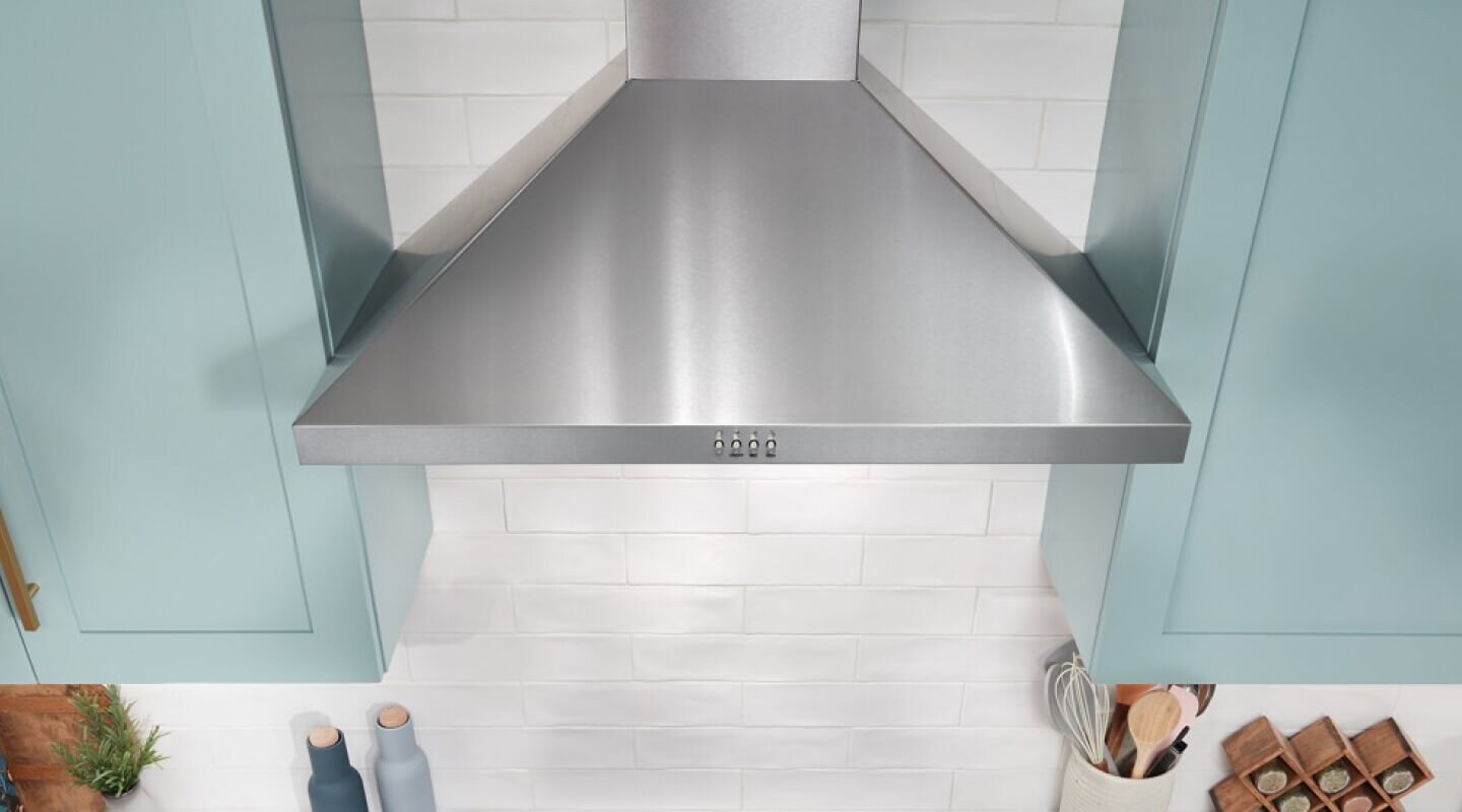 A stainless steel wall-mount range hood surrounded by light blue cabinetry
