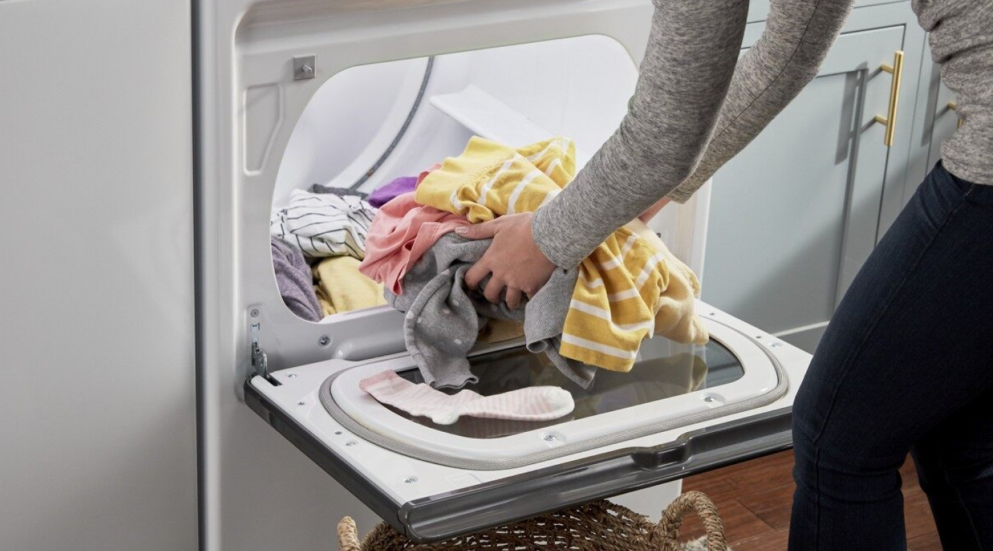 Person loading laundry into a dryer Person loading laundry into a dryer