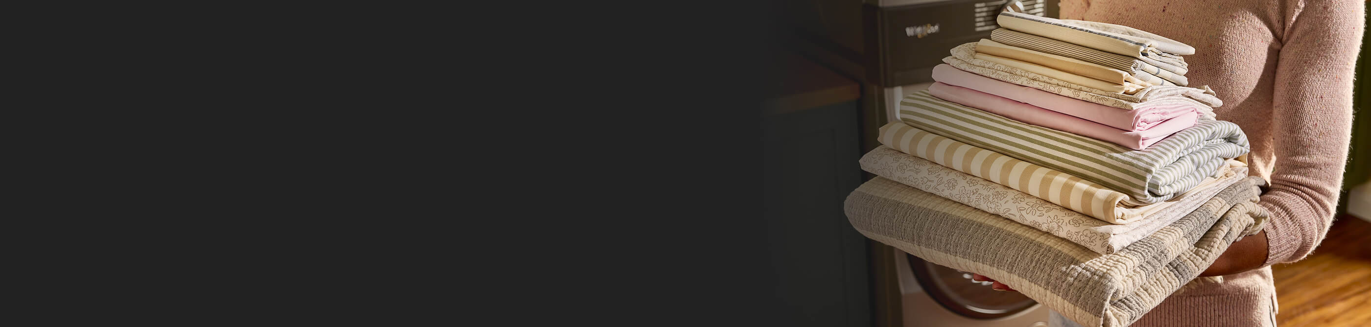 A person holding a stack of folded sheets and blankets