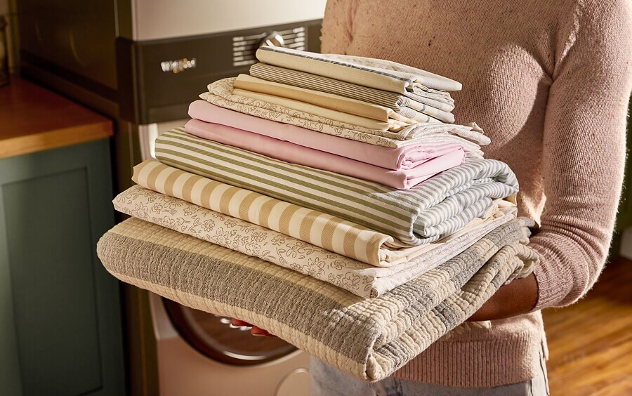 A person holding a stack of folded sheets and blankets