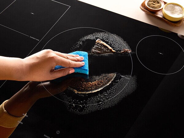 A person wiping the top of an electric cooktop clean
