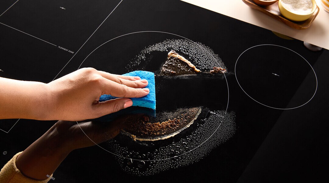 A person wiping the top of an electric cooktop clean