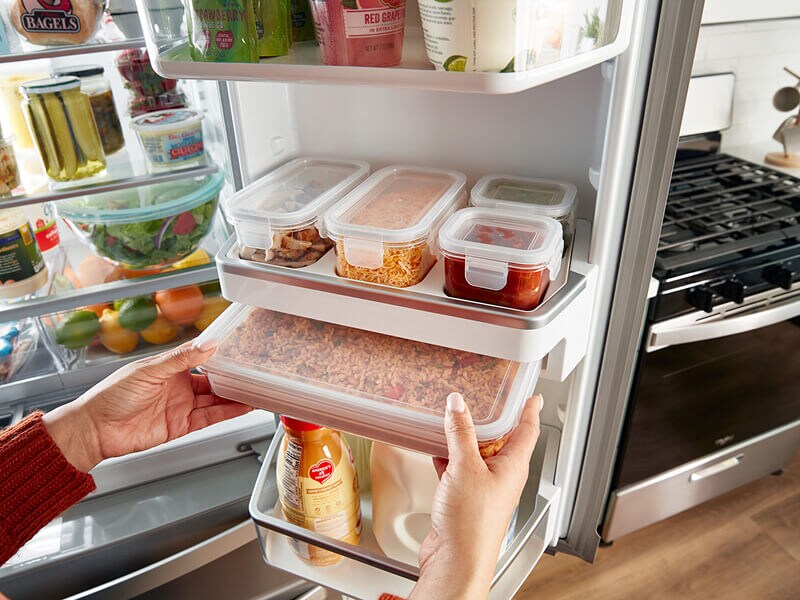 A person placing food stored in containers in a refrigerator 
