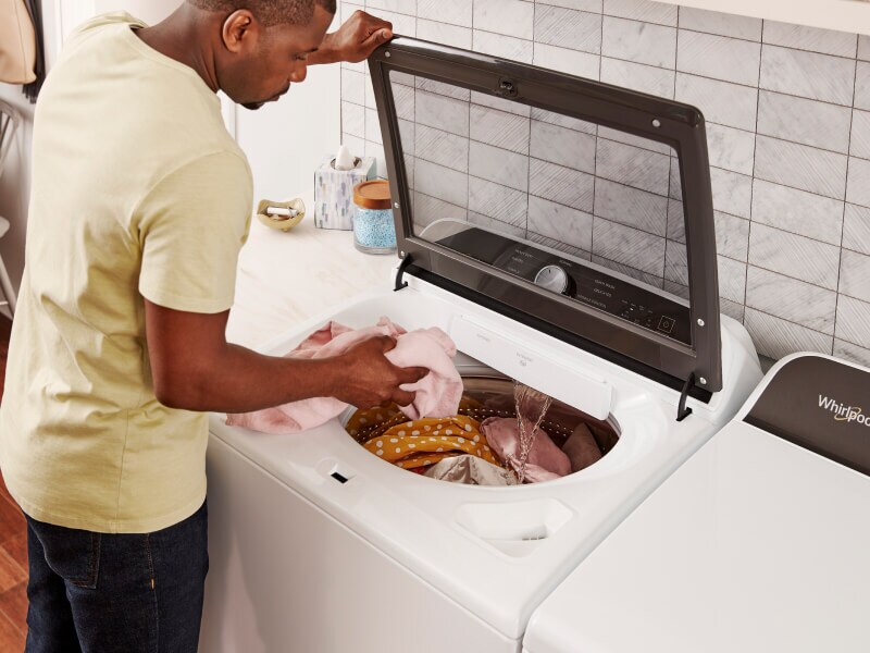 Man in a yellow shirt loading laundry into a top load washing machine from Whirlpool brand Man in a yellow shirt loading laundry into a top load washing machine from Whirlpool brand