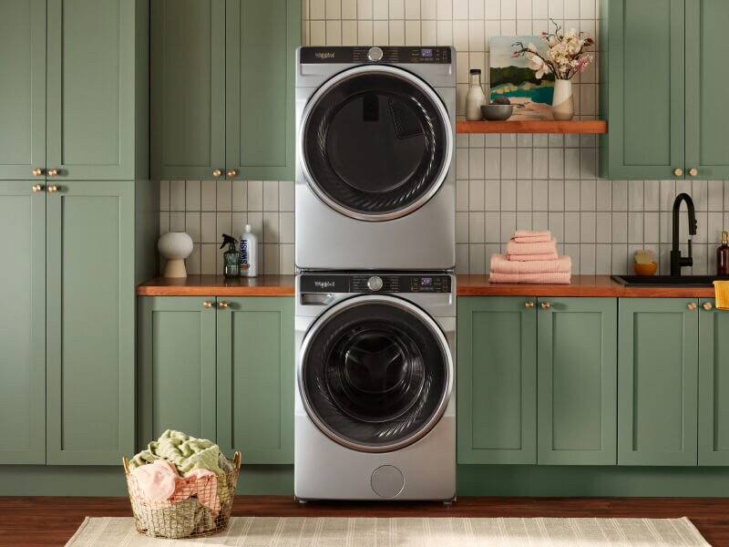 Stacked front load washer and dryer surrounded by green cabinets Stacked front load washer and dryer surrounded by green cabinets
