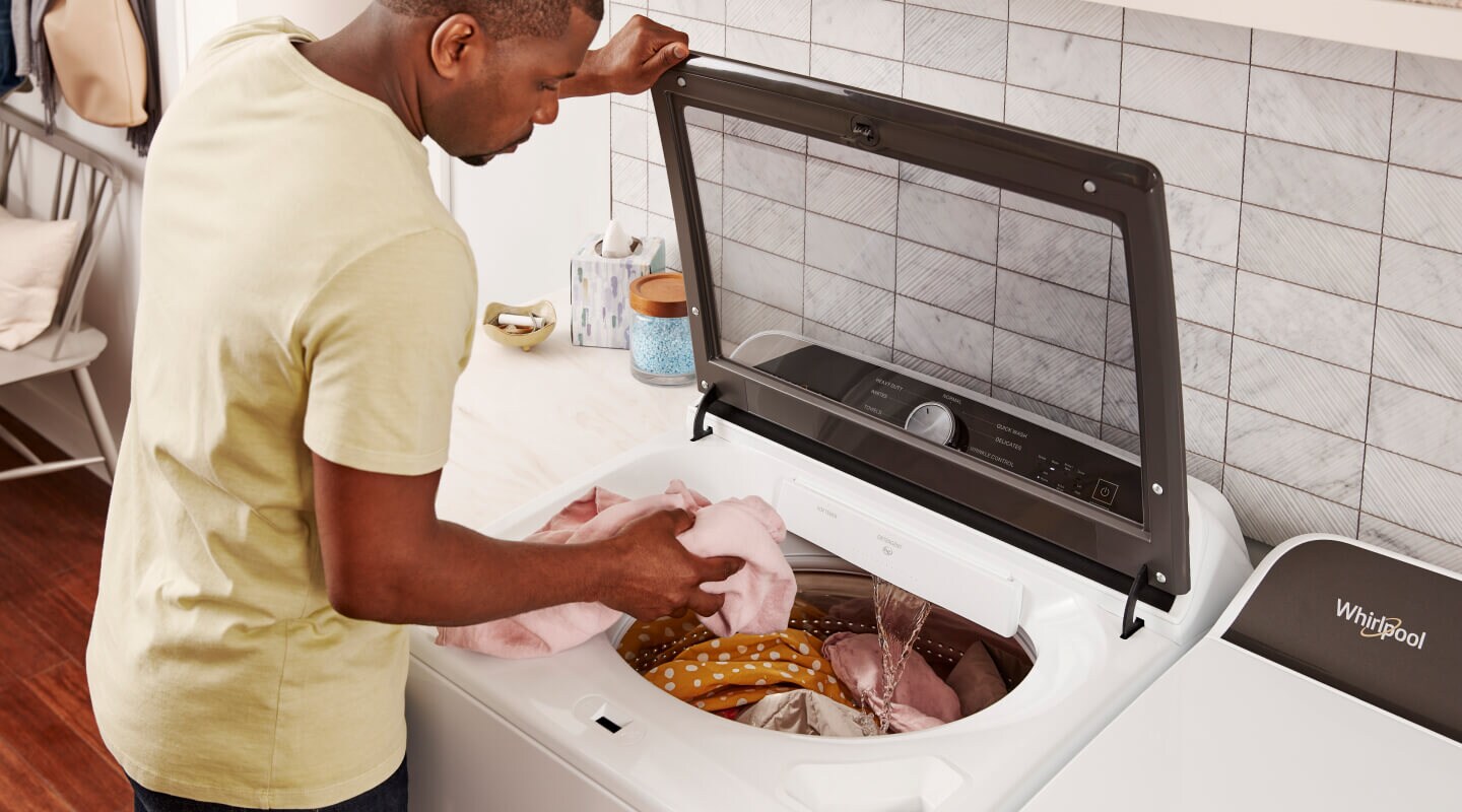 Man in a yellow shirt loading laundry into a top load washing machine from Whirlpool brand Man in a yellow shirt loading laundry into a top load washing machine from Whirlpool brand
