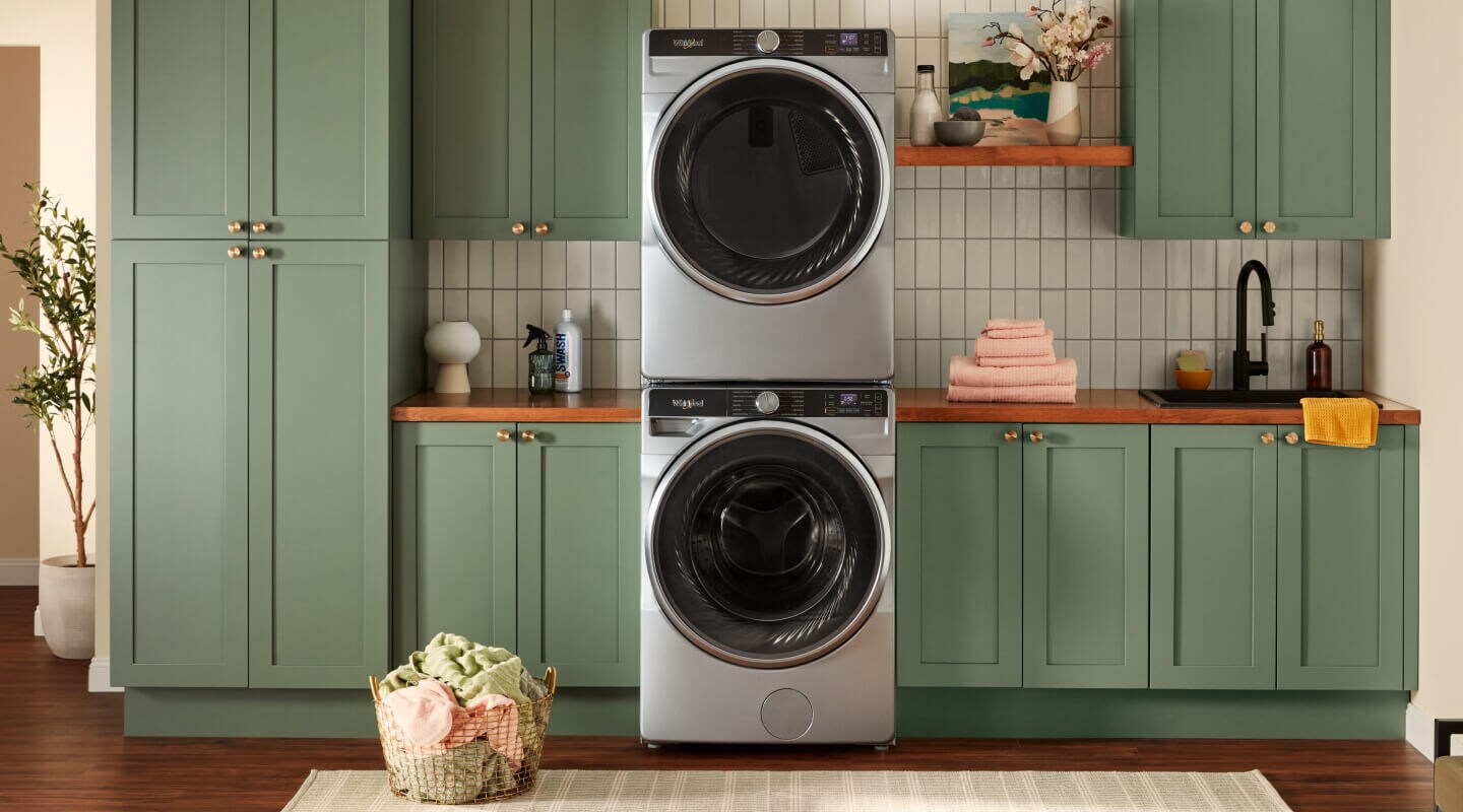 Stacked front load washer and dryer surrounded by green cabinets Stacked front load washer and dryer surrounded by green cabinets