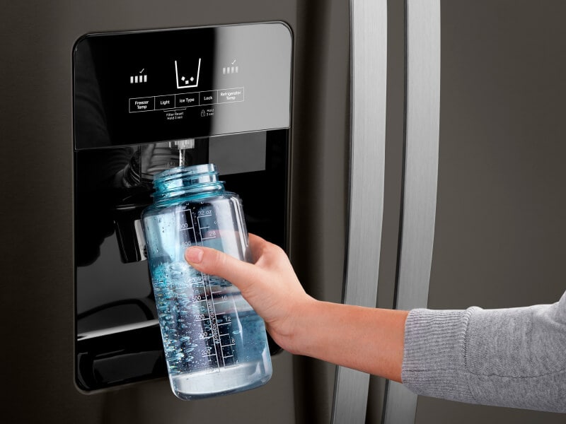Person using an in-door water dispenser on a fridge to fill a water bottle Person using an in-door water dispenser on a fridge to fill a water bottle