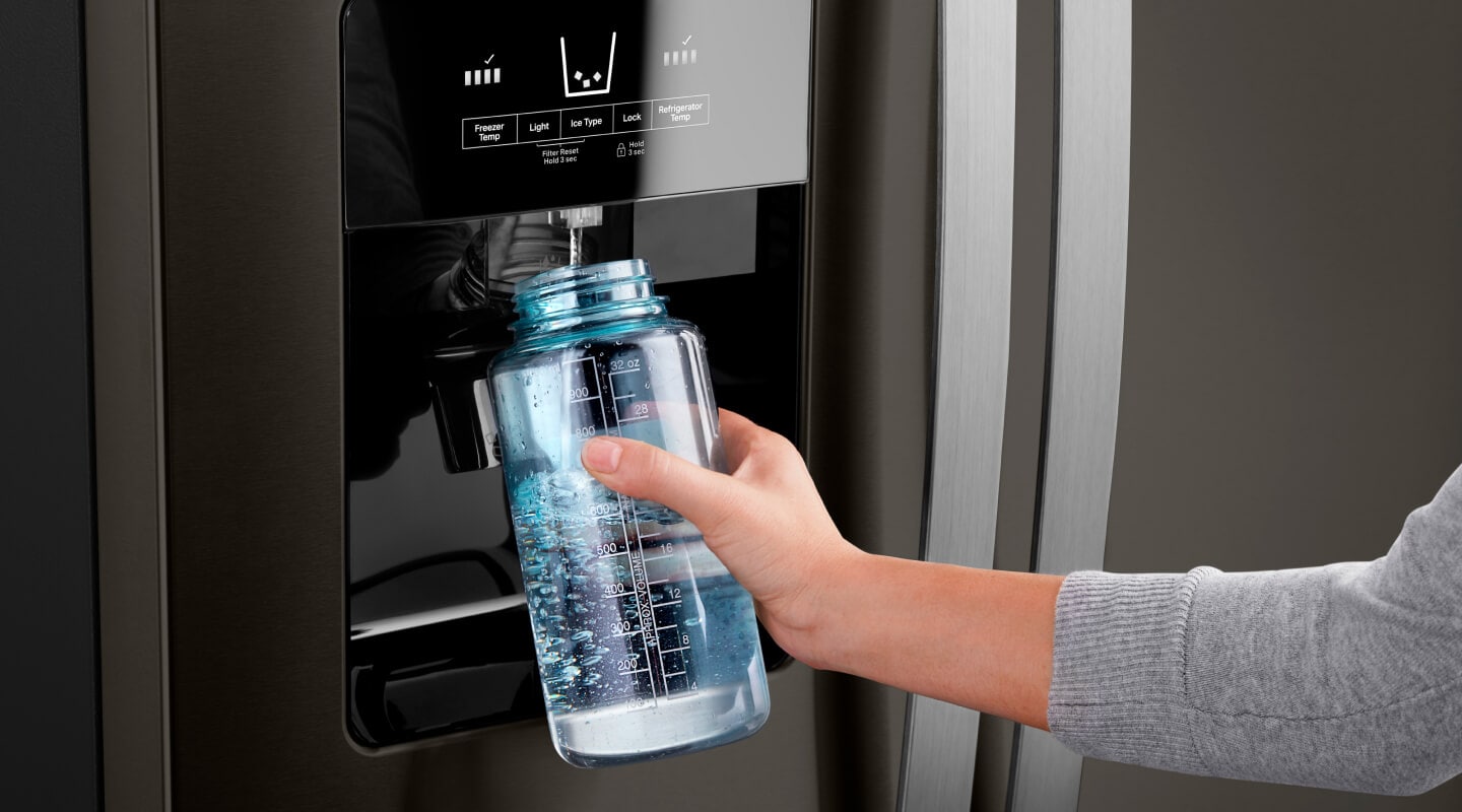 Person using an in-door water dispenser on a fridge to fill a water bottle Person using an in-door water dispenser on a fridge to fill a water bottle